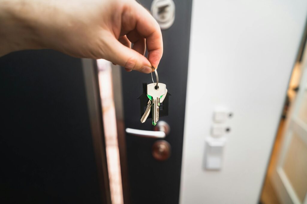 Close-up of a hand holding keys in front of an open door, symbolizing new homeownership.