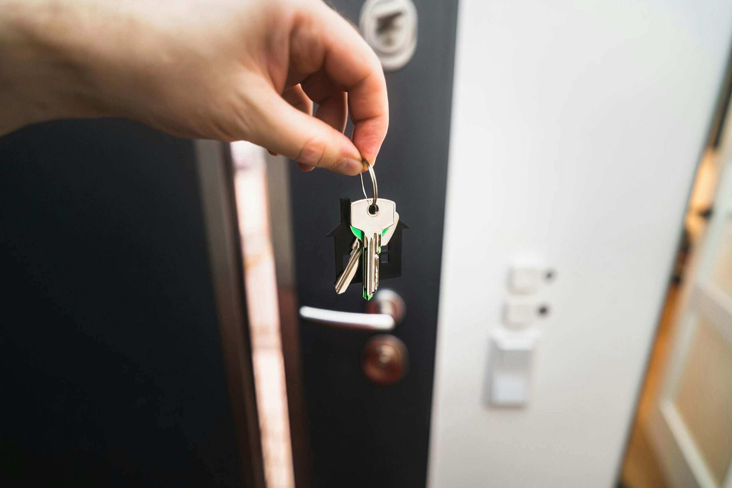 Close-up of a hand holding keys in front of an open door, symbolizing new homeownership.